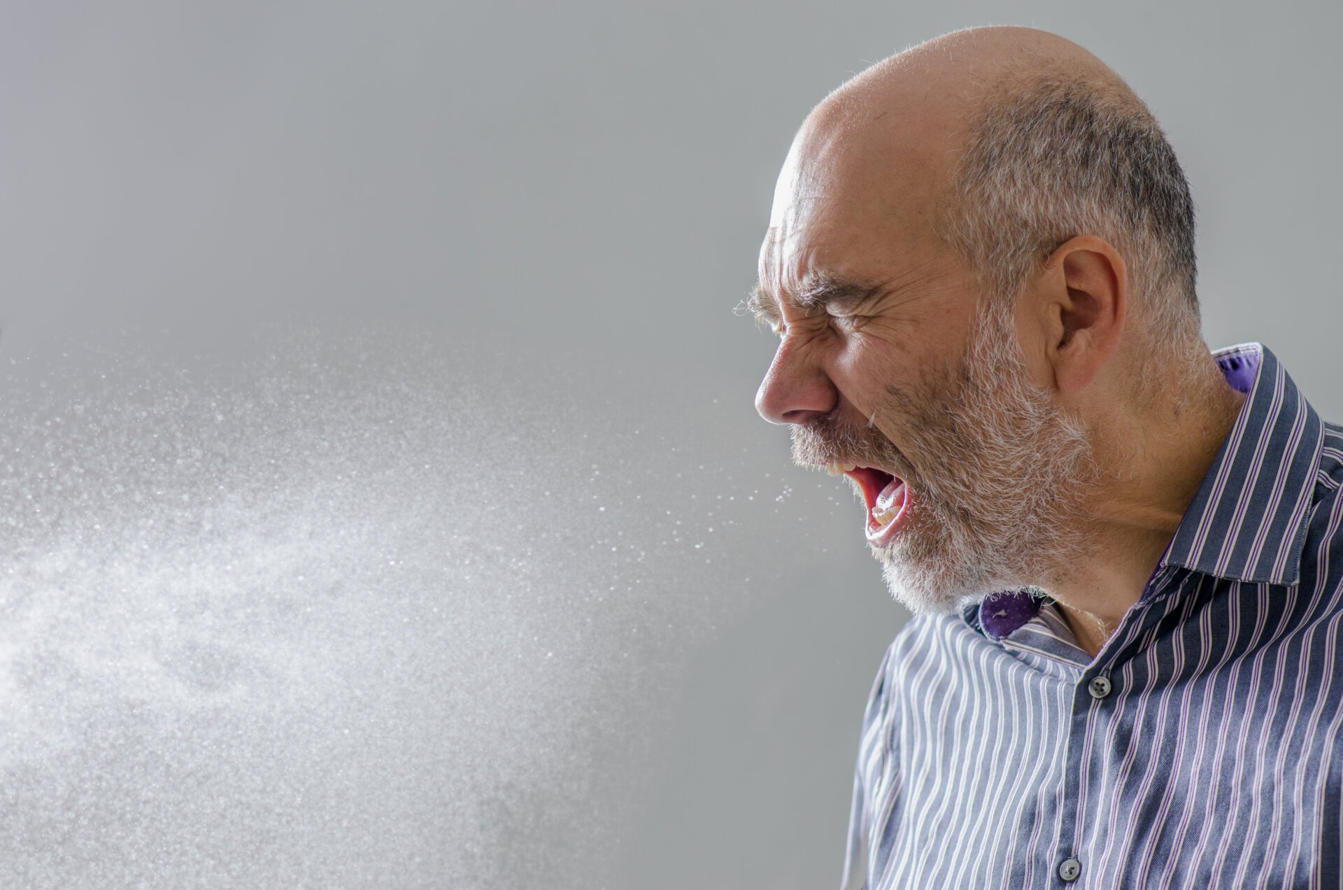 Man sneezing out a visible spray of water droplets.